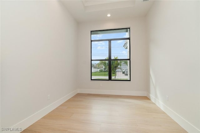 unfurnished room featuring light wood-type flooring, baseboards, a raised ceiling, and recessed lighting