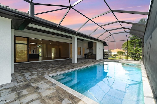 pool at dusk with a lanai, an outdoor pool, an outdoor kitchen, and a patio