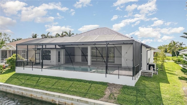 back of property featuring glass enclosure, a patio area, an outdoor pool, and a yard