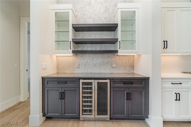 bar with light wood finished floors, beverage cooler, baseboards, and backsplash