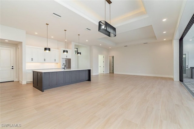 kitchen featuring white cabinets, a raised ceiling, open floor plan, hanging light fixtures, and light countertops