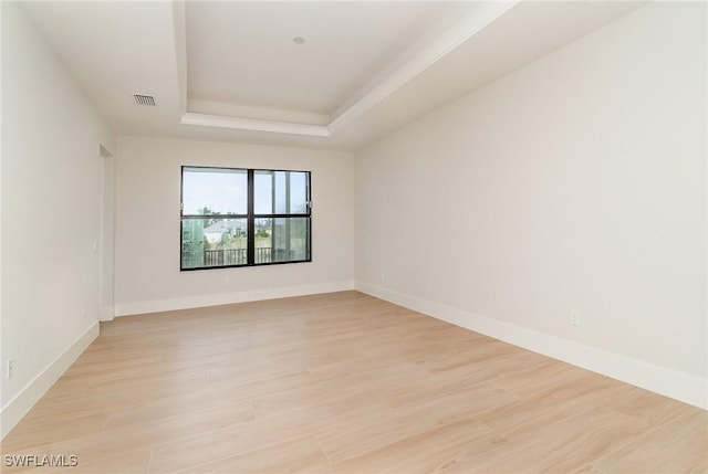 empty room with a tray ceiling, visible vents, light wood finished floors, and baseboards