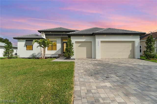 prairie-style home with a garage, decorative driveway, a yard, and stucco siding