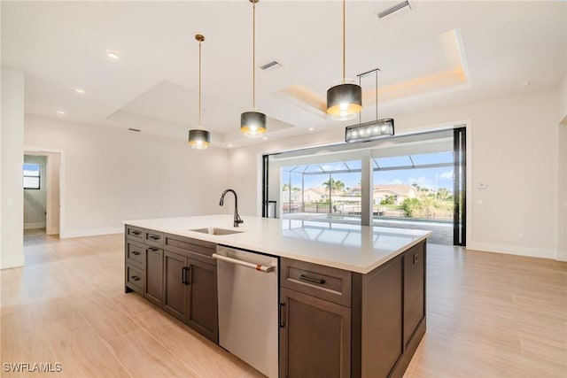 kitchen featuring a sink, light countertops, stainless steel dishwasher, and a raised ceiling