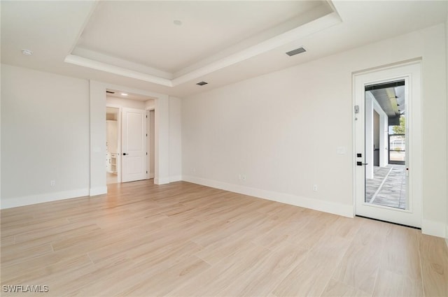 spare room with light wood-type flooring, a raised ceiling, visible vents, and baseboards