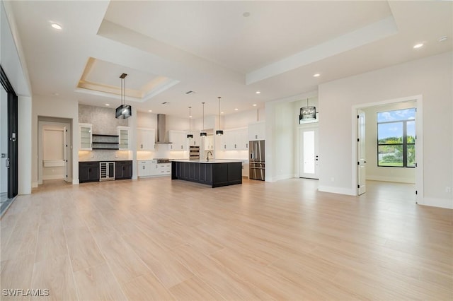 unfurnished living room featuring light wood-style flooring, recessed lighting, a sink, baseboards, and a raised ceiling