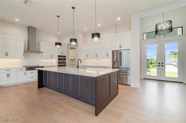 kitchen featuring wall chimney range hood, white cabinetry, appliances with stainless steel finishes, and light countertops