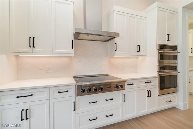 kitchen with stainless steel appliances, light countertops, backsplash, white cabinets, and wall chimney range hood