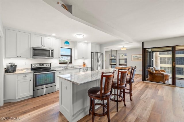 kitchen with a sink, stainless steel appliances, white cabinets, light wood-style floors, and a kitchen bar