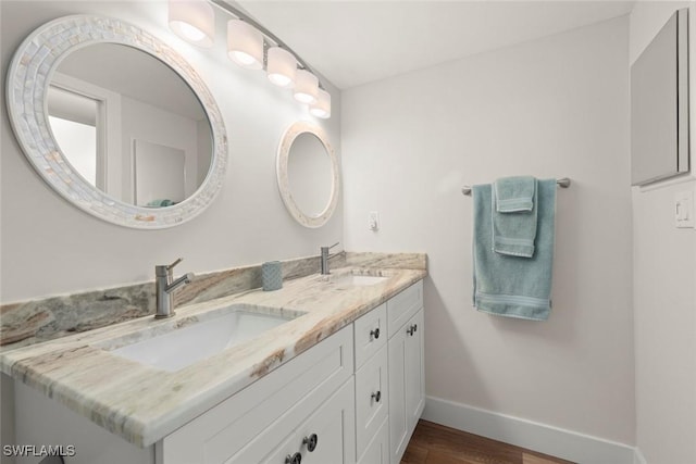 bathroom with a sink, baseboards, wood finished floors, and double vanity