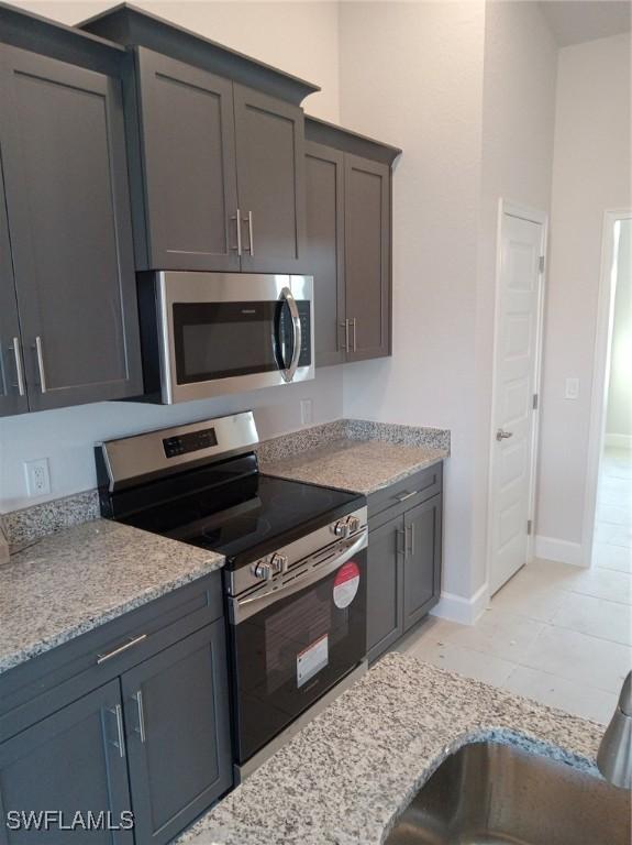 kitchen with baseboards, stainless steel appliances, light tile patterned floors, and light stone countertops