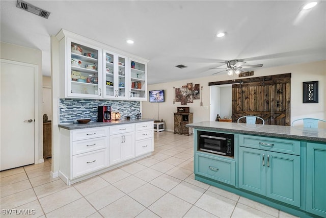 kitchen featuring black microwave, white cabinets, backsplash, dark countertops, and glass insert cabinets