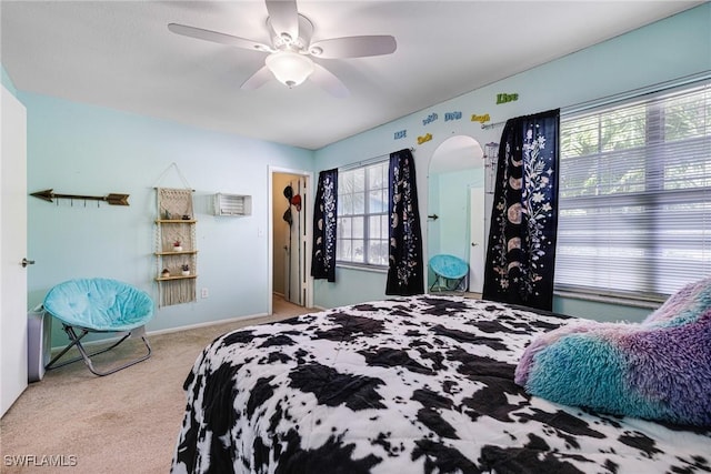 bedroom with light carpet, ceiling fan, arched walkways, and baseboards