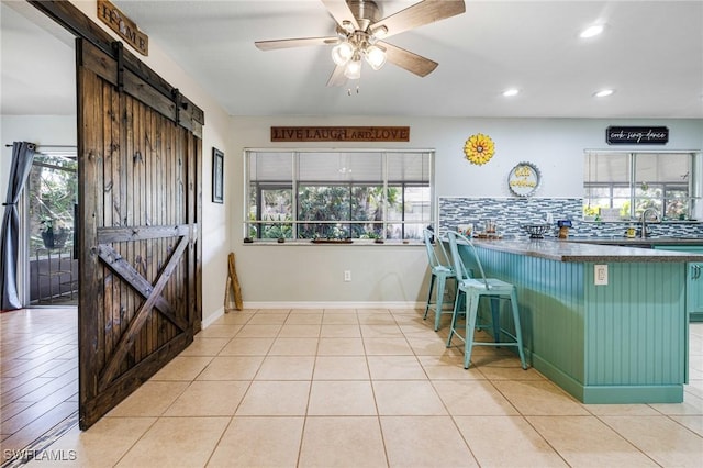 kitchen featuring dark countertops, decorative backsplash, green cabinets, a barn door, and ceiling fan