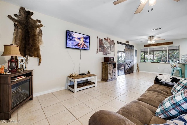 living area with light tile patterned floors, a barn door, visible vents, baseboards, and a ceiling fan