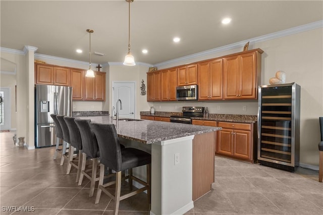 kitchen with wine cooler, brown cabinets, a kitchen island with sink, stainless steel appliances, and a sink