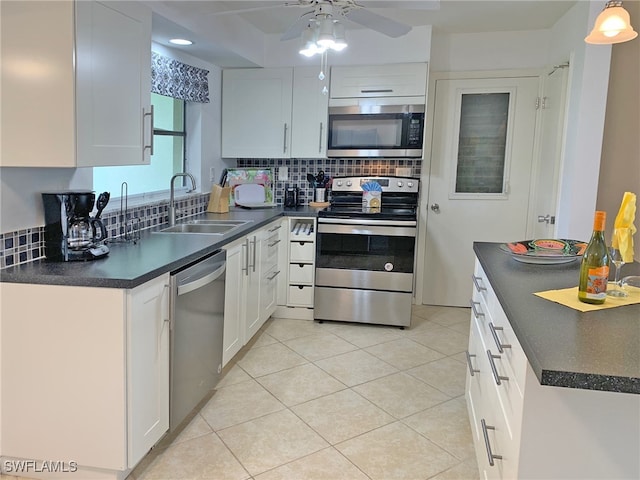 kitchen with stainless steel appliances, dark countertops, a sink, and white cabinets