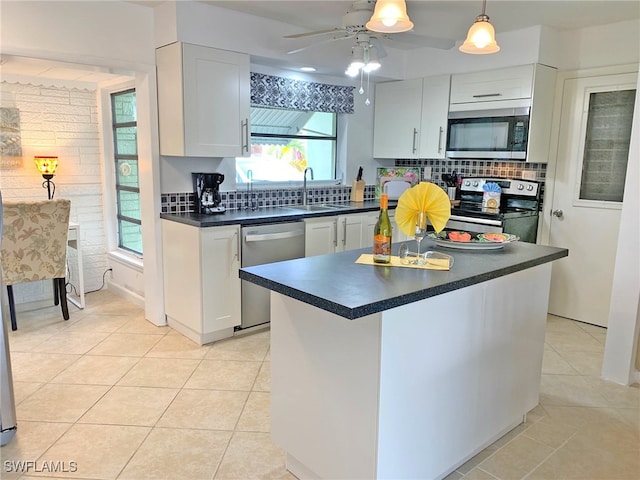 kitchen featuring white cabinets, dark countertops, a center island, stainless steel appliances, and a sink