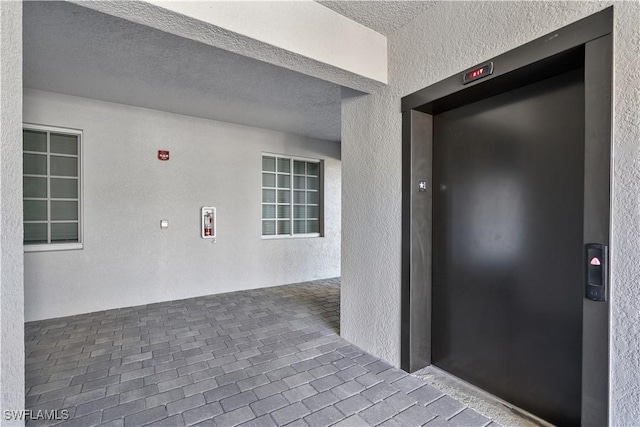 hall with elevator, brick floor, a textured ceiling, and a textured wall