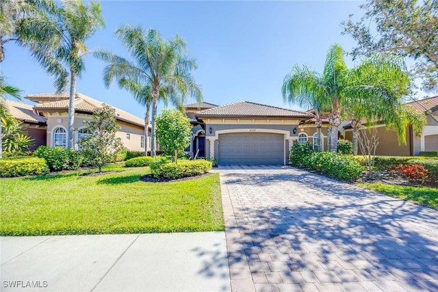 mediterranean / spanish house featuring decorative driveway, a tile roof, stucco siding, a front yard, and a garage