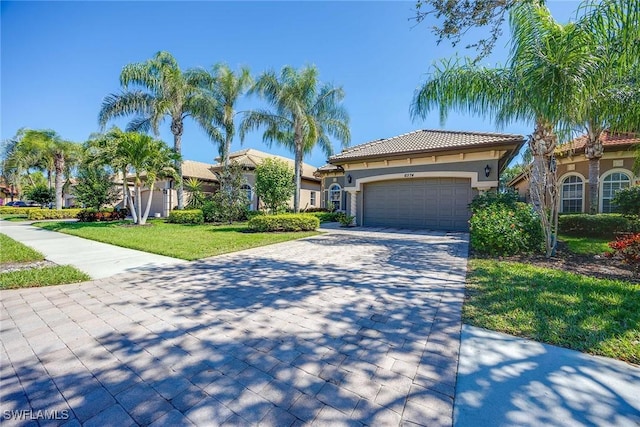 mediterranean / spanish-style house featuring decorative driveway, stucco siding, an attached garage, a tiled roof, and a front lawn