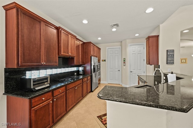 kitchen featuring stainless steel fridge, visible vents, dark stone counters, a peninsula, and a sink