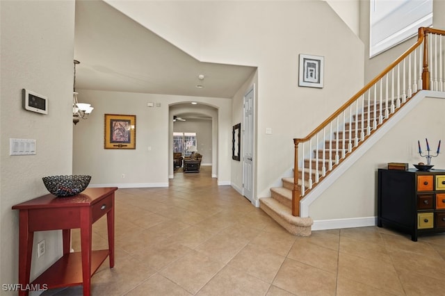 foyer entrance featuring stairs, arched walkways, baseboards, and light tile patterned floors