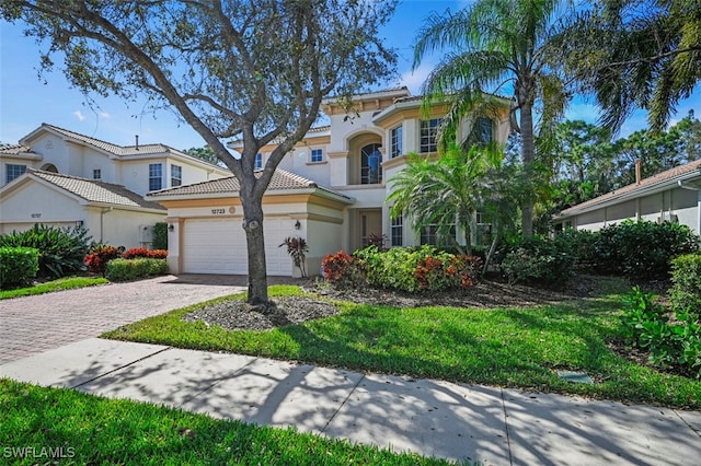 mediterranean / spanish house featuring a garage, a tile roof, decorative driveway, and stucco siding