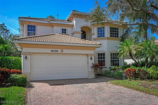 mediterranean / spanish-style home featuring decorative driveway, a tiled roof, an attached garage, and stucco siding