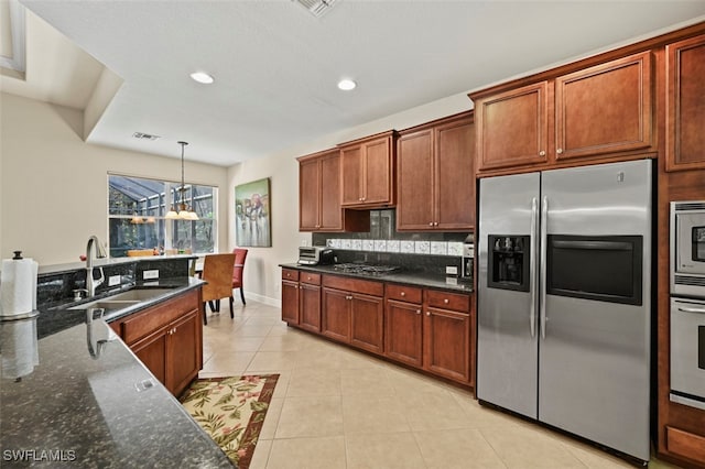 kitchen with light tile patterned floors, a sink, hanging light fixtures, appliances with stainless steel finishes, and dark stone countertops