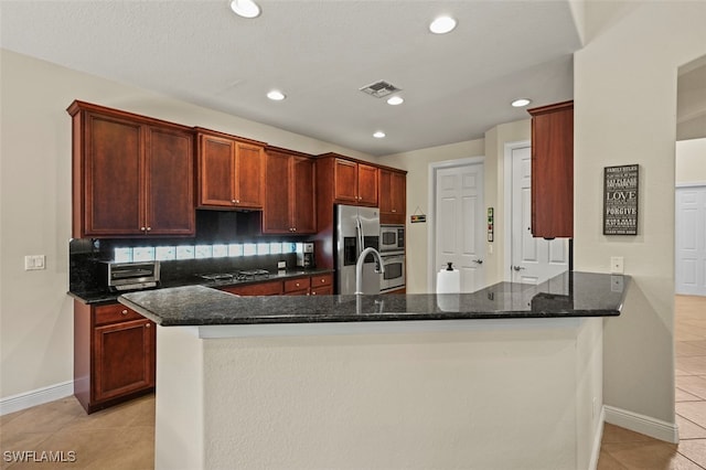 kitchen featuring light tile patterned floors, a peninsula, stainless steel appliances, visible vents, and dark stone counters