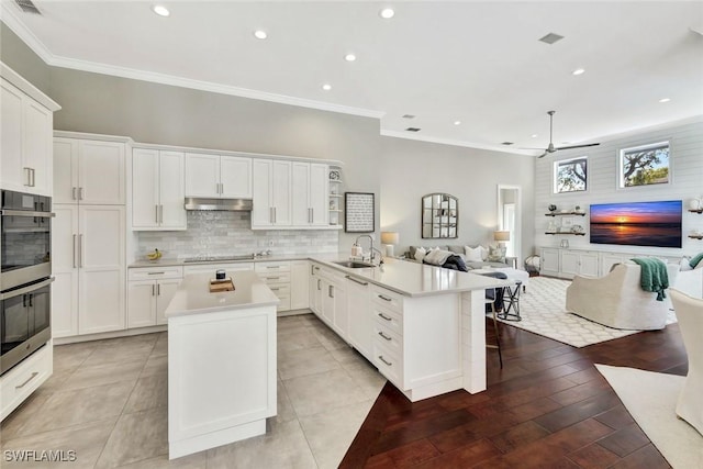 kitchen with black electric cooktop, under cabinet range hood, a peninsula, a sink, and open floor plan