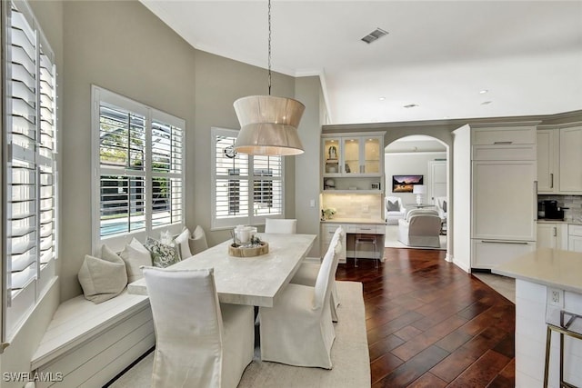 dining room with dark wood-style floors, visible vents, arched walkways, and crown molding