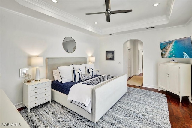 bedroom featuring arched walkways, a tray ceiling, wood finished floors, and ornamental molding