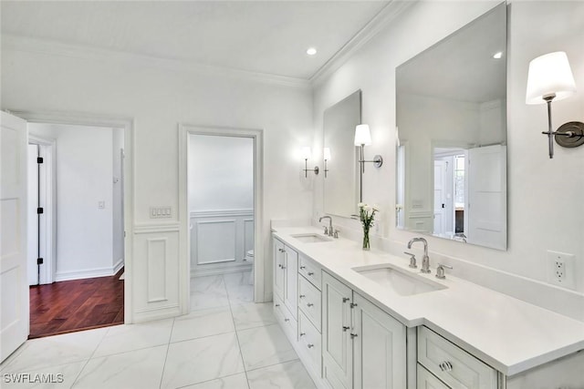 bathroom with toilet, marble finish floor, ornamental molding, and a sink