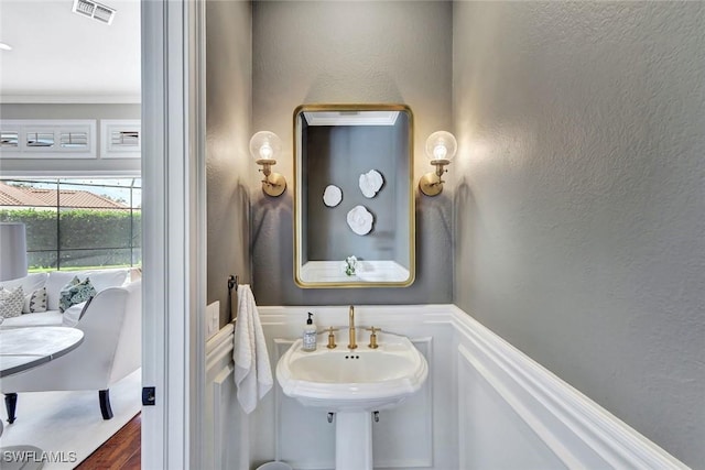 bathroom featuring visible vents, a textured wall, a wainscoted wall, wood finished floors, and crown molding