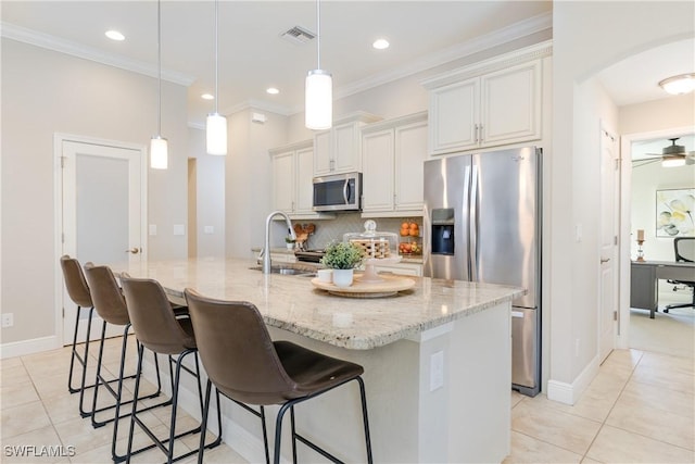 kitchen with white cabinets, appliances with stainless steel finishes, light stone countertops, an island with sink, and pendant lighting