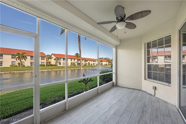 unfurnished sunroom with a ceiling fan, a residential view, and a water view