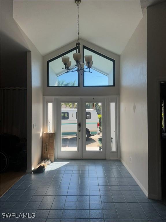 entryway with tile patterned flooring, a notable chandelier, french doors, and high vaulted ceiling