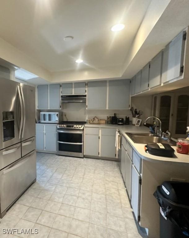 kitchen featuring gray cabinets, a sink, stainless steel appliances, light countertops, and under cabinet range hood