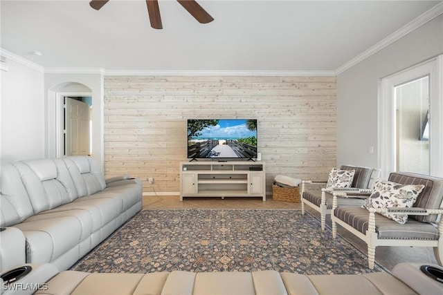 living area featuring light tile patterned floors, an accent wall, ornamental molding, and a ceiling fan