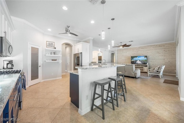 kitchen with arched walkways, white cabinetry, a center island with sink, and pendant lighting