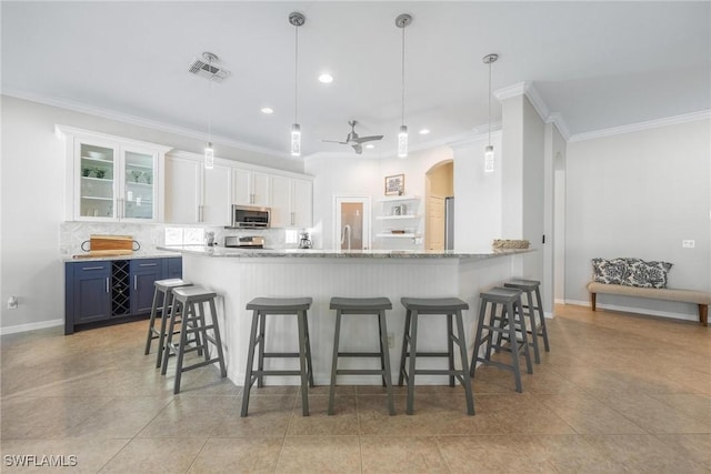 kitchen featuring pendant lighting, a breakfast bar area, blue cabinetry, stainless steel microwave, and white cabinetry