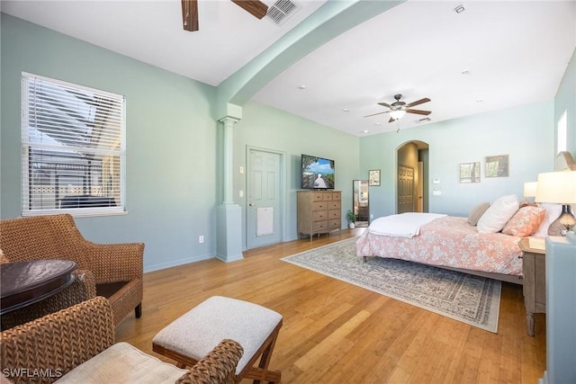 bedroom with arched walkways, a ceiling fan, visible vents, light wood-style floors, and decorative columns