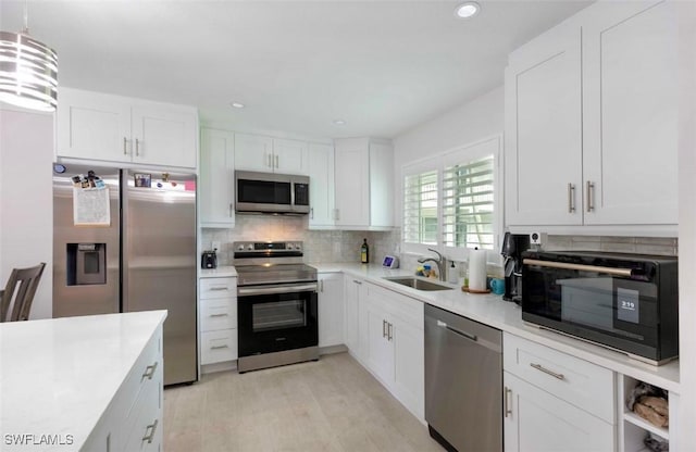 kitchen featuring stainless steel appliances, a sink, white cabinets, light countertops, and backsplash