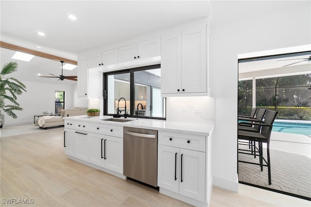 kitchen featuring light countertops, a sink, stainless steel dishwasher, and white cabinetry