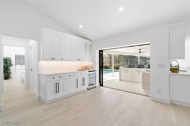 kitchen featuring wine cooler, light wood finished floors, light countertops, white cabinetry, and a sink