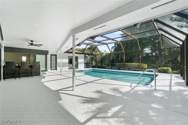 outdoor pool with a patio area, glass enclosure, ceiling fan, and a bar