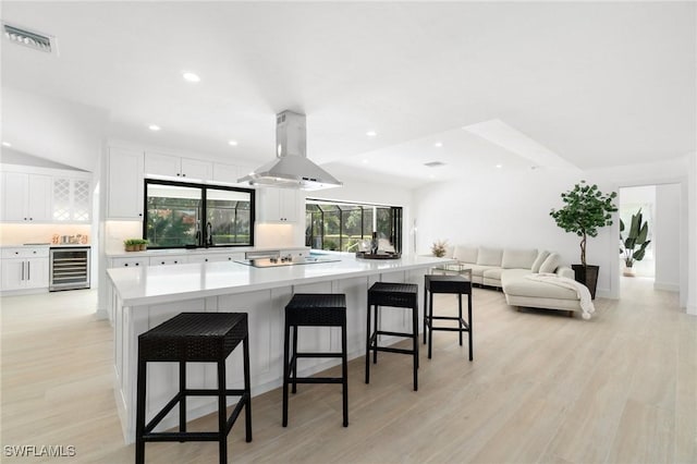 kitchen with beverage cooler, a breakfast bar area, island exhaust hood, and white cabinets