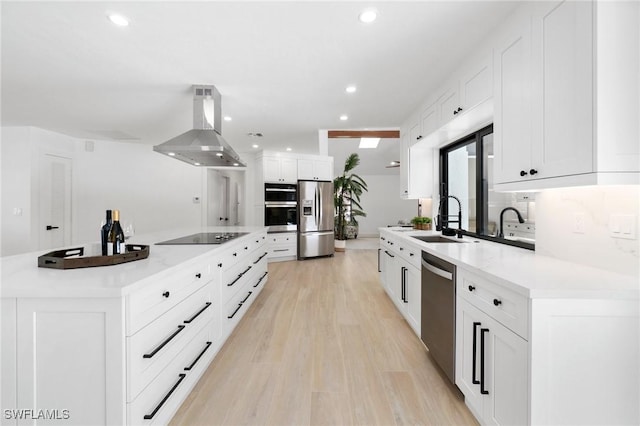 kitchen with island range hood, white cabinets, stainless steel appliances, light countertops, and a sink